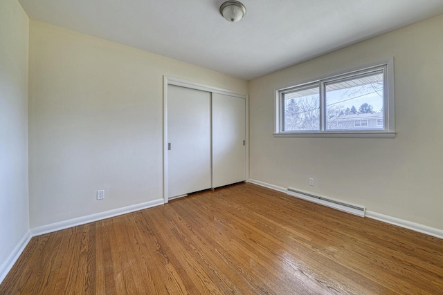 unfurnished bedroom with a baseboard heating unit, wood finished floors, baseboards, and a closet