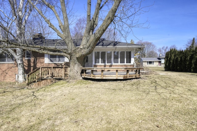 back of house with brick siding, a lawn, a chimney, and a deck