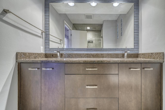 bathroom featuring a sink, visible vents, tiled shower, and double vanity