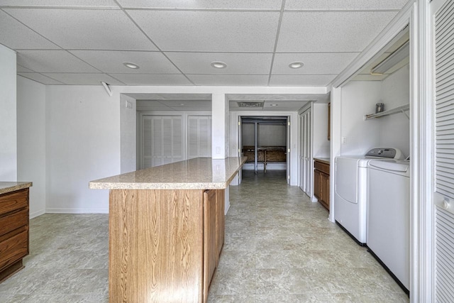 kitchen featuring baseboards, washing machine and dryer, light countertops, brown cabinetry, and a paneled ceiling