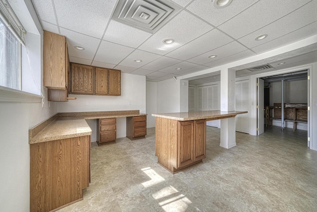 kitchen featuring a paneled ceiling, a center island, brown cabinetry, and light countertops