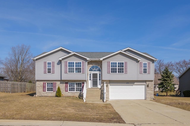 split foyer home with a front yard, fence, an attached garage, concrete driveway, and brick siding