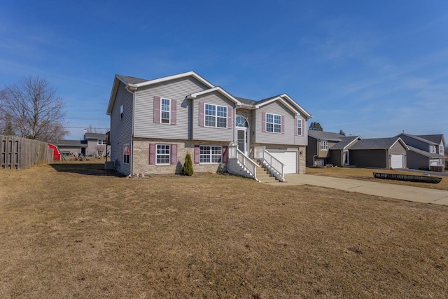 raised ranch featuring a front yard, fence, driveway, an attached garage, and brick siding