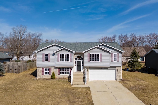 raised ranch featuring brick siding, fence, concrete driveway, a front yard, and a garage