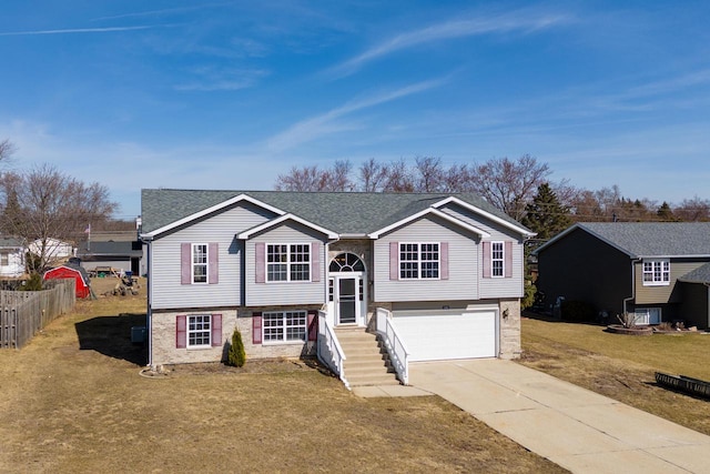 raised ranch with fence, concrete driveway, a front yard, an attached garage, and central AC unit