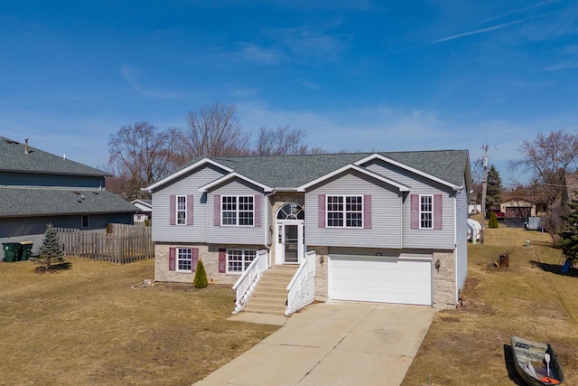 raised ranch featuring fence, concrete driveway, a front lawn, a garage, and brick siding