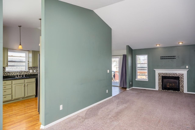 unfurnished living room with baseboards, lofted ceiling, a sink, a tile fireplace, and light carpet