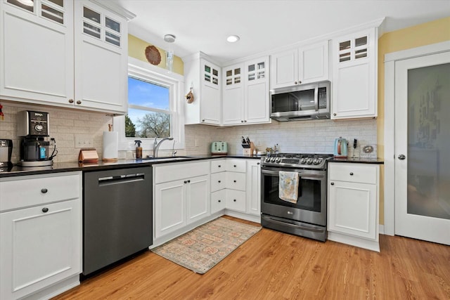 kitchen featuring dark countertops, light wood-style floors, white cabinets, stainless steel appliances, and a sink