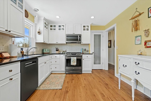 kitchen featuring light wood-style flooring, a sink, stainless steel appliances, white cabinets, and backsplash