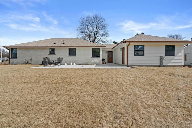 rear view of property featuring a patio, a lawn, brick siding, and a shingled roof