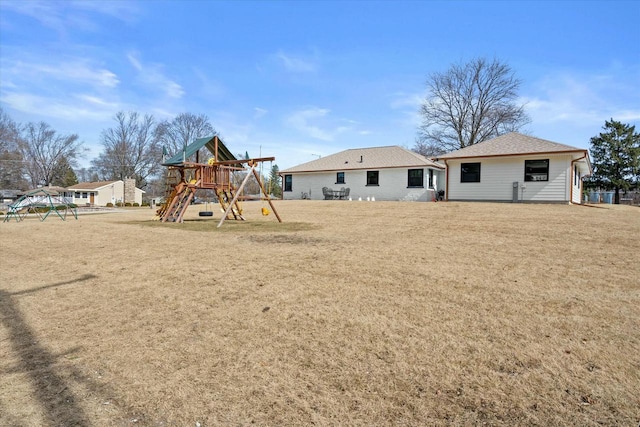 rear view of house featuring a shingled roof, a playground, and a yard