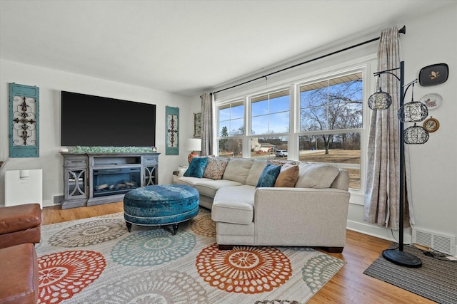 living area featuring a glass covered fireplace, visible vents, baseboards, and wood finished floors