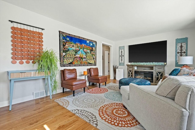 living room with a glass covered fireplace, visible vents, baseboards, and wood finished floors