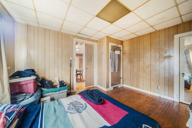 bedroom with wooden walls, a paneled ceiling, and hardwood / wood-style flooring