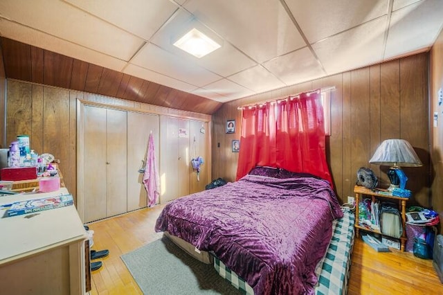 bedroom with wooden walls, a drop ceiling, and hardwood / wood-style floors