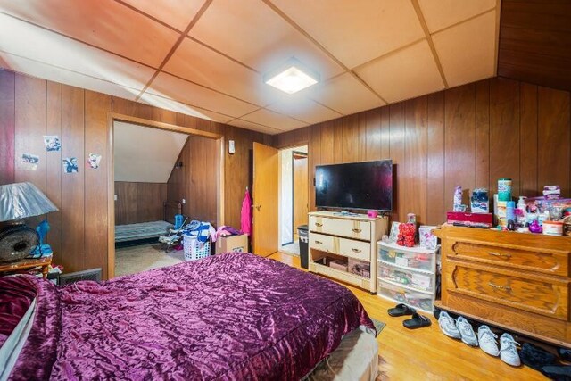 bedroom featuring a paneled ceiling, wooden walls, and wood finished floors