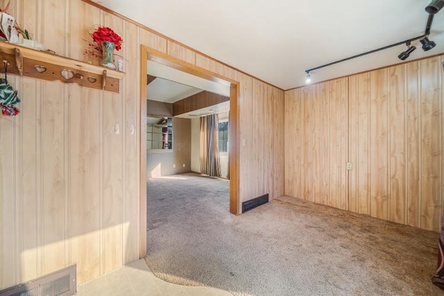 carpeted spare room featuring visible vents, wood walls, and track lighting