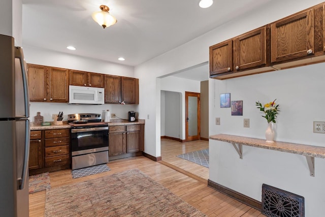 kitchen featuring light stone counters, recessed lighting, appliances with stainless steel finishes, light wood finished floors, and baseboards