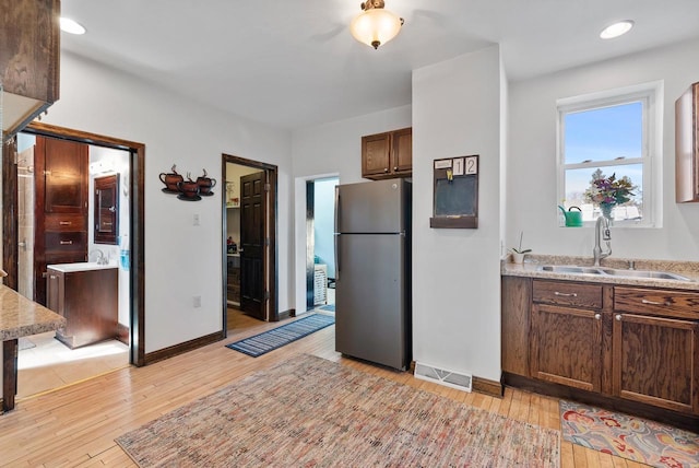 kitchen with a sink, light wood-style flooring, light countertops, and freestanding refrigerator