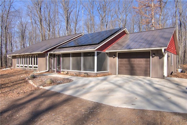 single story home with concrete driveway, an attached garage, a sunroom, metal roof, and solar panels