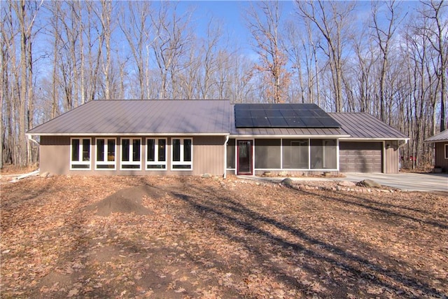 ranch-style house with solar panels, an attached garage, a sunroom, concrete driveway, and metal roof