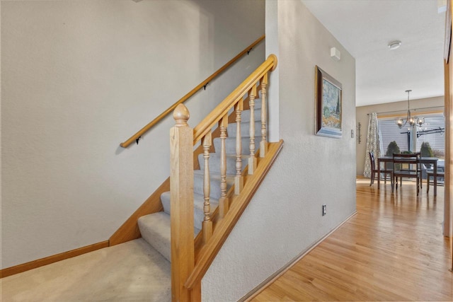 stairs featuring wood finished floors, baseboards, a textured wall, and a chandelier