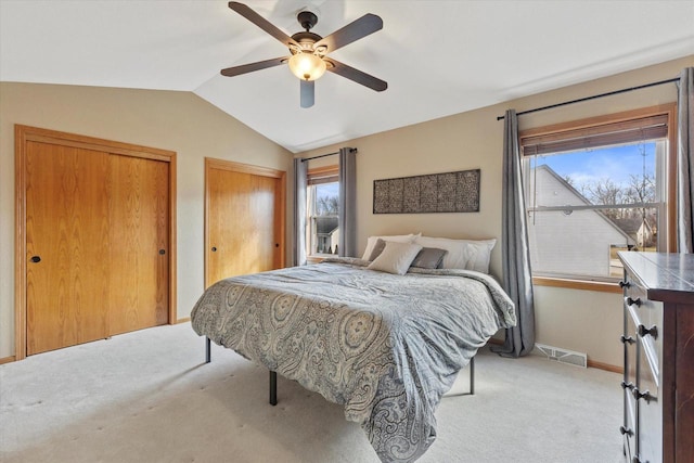 bedroom featuring visible vents, multiple closets, baseboards, lofted ceiling, and light colored carpet