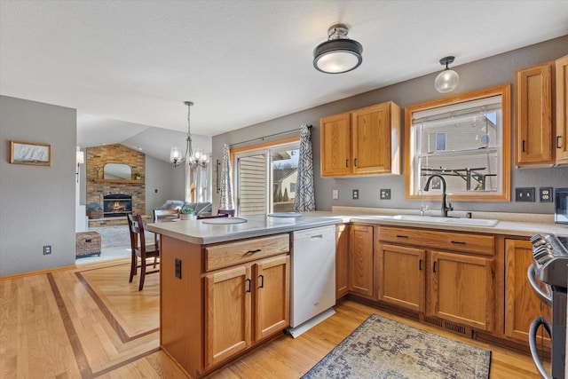 kitchen with a sink, a peninsula, stainless steel stove, a brick fireplace, and dishwasher