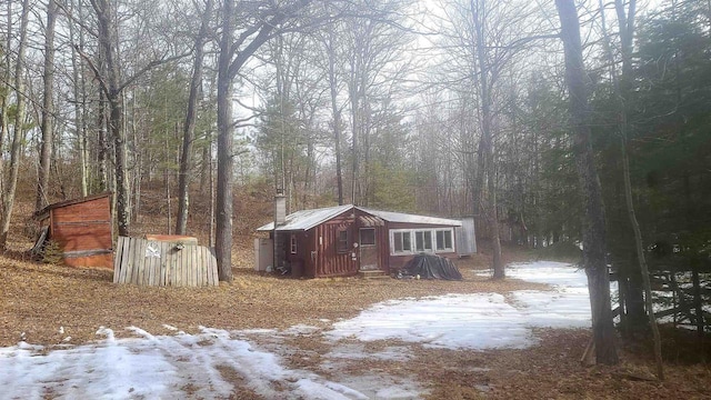 snow covered structure with a wooded view and an outdoor structure