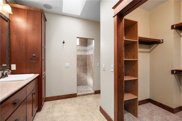 bathroom featuring baseboards, walk in shower, a skylight, and vanity