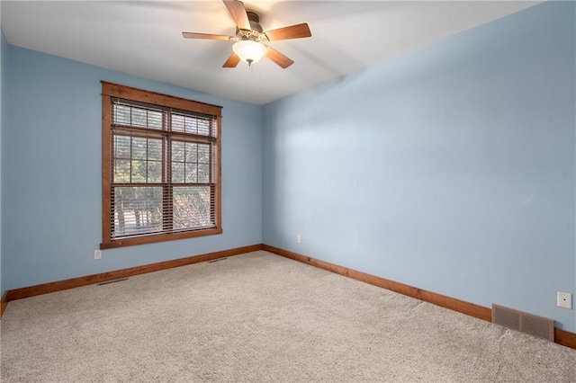 carpeted spare room with visible vents, a ceiling fan, and baseboards