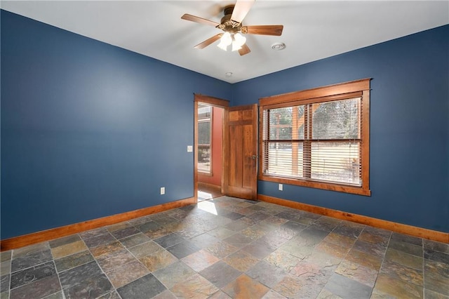 empty room with baseboards, stone tile floors, and ceiling fan