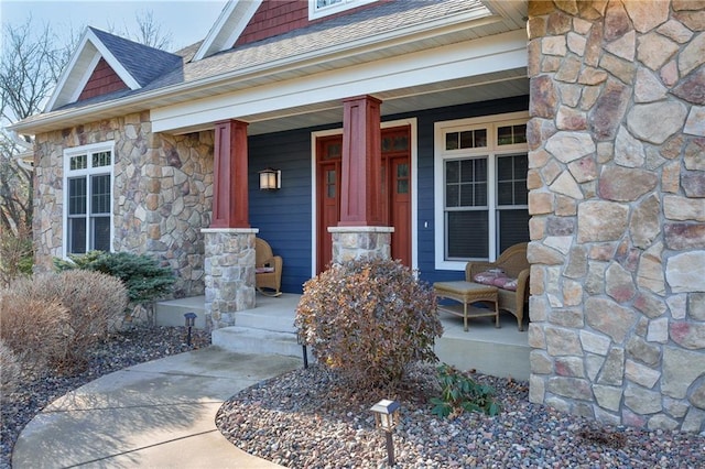 view of exterior entry featuring stone siding, a porch, and a shingled roof