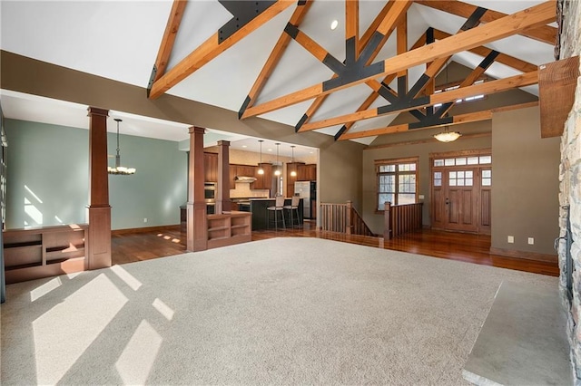 unfurnished living room with wood finished floors, baseboards, ornate columns, high vaulted ceiling, and beamed ceiling