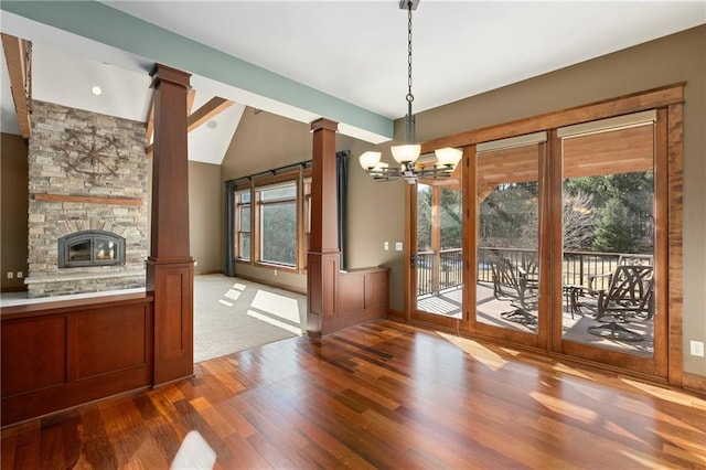 unfurnished dining area with a notable chandelier, wood finished floors, a fireplace, decorative columns, and lofted ceiling