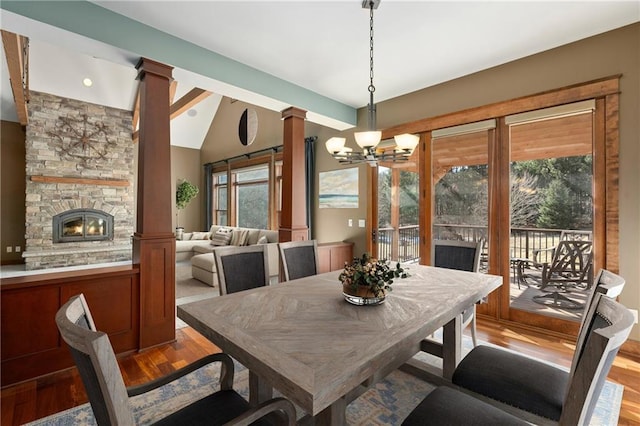 dining area featuring a notable chandelier, light wood-style floors, a fireplace, lofted ceiling, and ornate columns