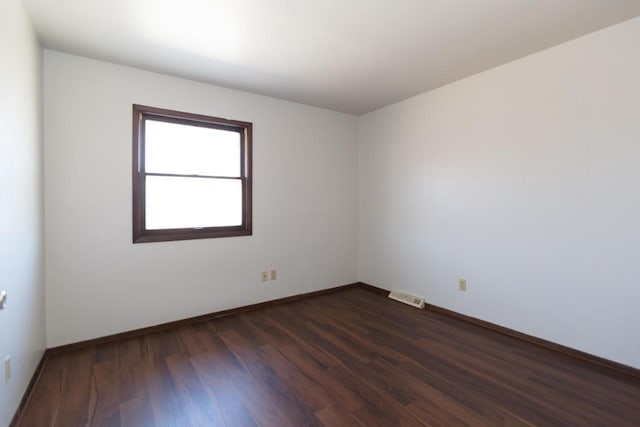 unfurnished room featuring visible vents, dark wood-type flooring, and baseboards