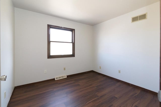 empty room featuring dark wood-type flooring, baseboards, and visible vents