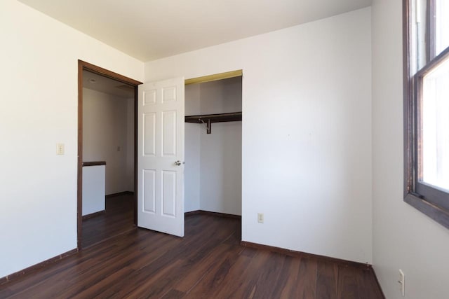 unfurnished bedroom with dark wood finished floors, baseboards, and a closet