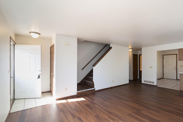 unfurnished living room featuring visible vents, baseboards, wood finished floors, and stairs