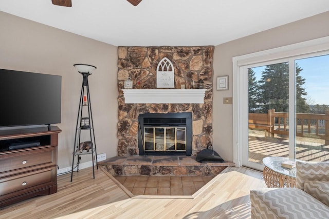 living area with ceiling fan, baseboards, a stone fireplace, and wood finished floors