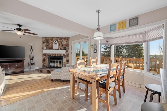 dining space featuring a fireplace, baseboards, light wood-type flooring, and ceiling fan