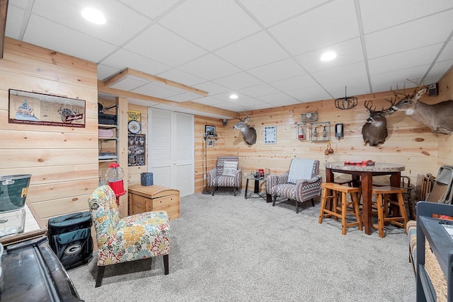 carpeted living room featuring recessed lighting, a drop ceiling, and wooden walls