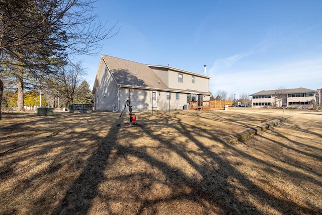 back of property featuring a wooden deck, a lawn, and a shingled roof