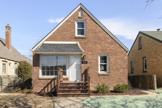 view of front of house with fence, brick siding, and a shingled roof