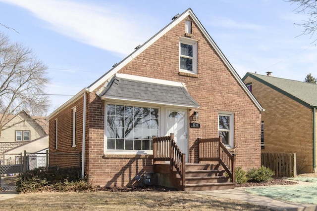 view of front of home featuring brick siding, a shingled roof, and fence