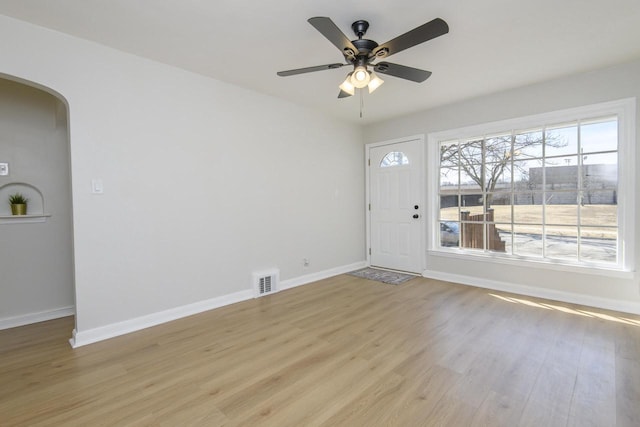 entrance foyer with a ceiling fan, visible vents, baseboards, arched walkways, and light wood-style floors