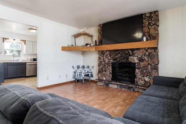 living room with light wood finished floors, a stone fireplace, and baseboards