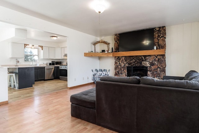 living area with a stone fireplace, baseboards, and light wood-type flooring