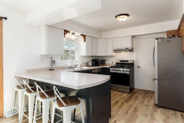 kitchen with under cabinet range hood, appliances with stainless steel finishes, a peninsula, white cabinetry, and a sink